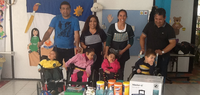 Group of adults and children with disabilities smiling, with various donations on a table in front.